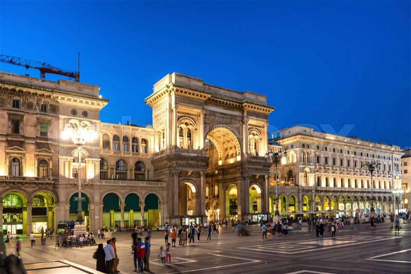 People walking near Vittorio Emanuele II gallery at Duomo square, Milan, Italy. Night view of street and buildings, stock photo