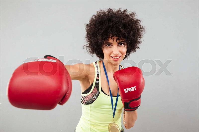 Smiling carefree sports woman boxing at the camera over gray background, stock photo