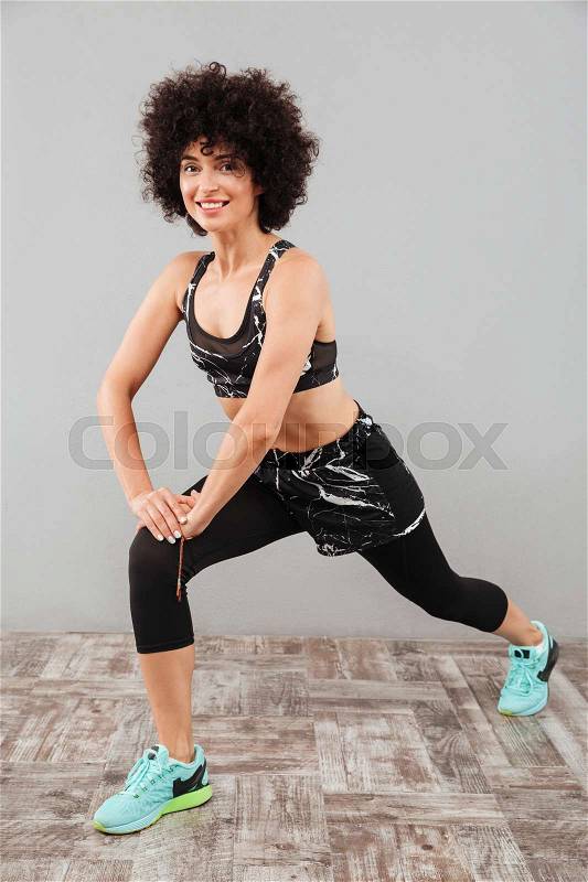Vertical image of Smiling sports woman stretching and looking at the camera over gray background, stock photo