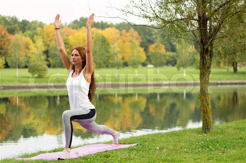 Young attractive woman practicing yoga, standing in Warrior one exercise, Virabhadrasana I pose, working out, stock photo