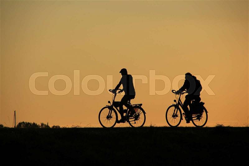 The couple, man and wife are biking on the dyke in the park in the village Hellevoetsluis at sunset in autumn, stock photo