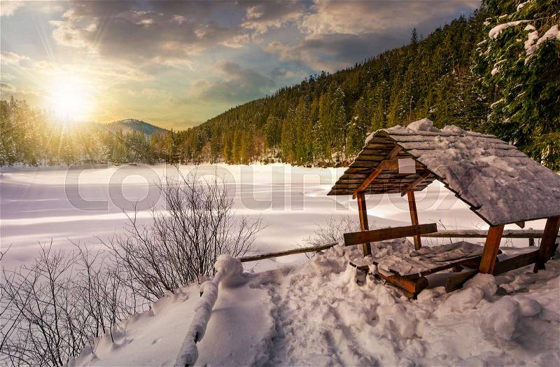 Wooden bower in snowy winter spruce forest. beautiful mountainous landscape near snow covered frozen lake at sunset, stock photo