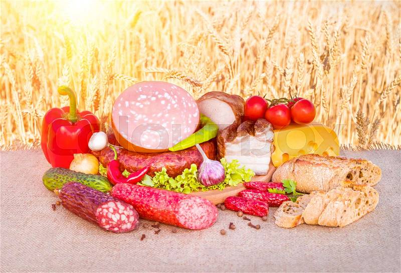 Meat products. Smoked ham, sausage, bacon, vegetables lying on a table in a wheat field, stock photo