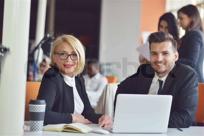 Beautiful young business partners are using a laptop, discussing documents and smiling while working in office, stock photo