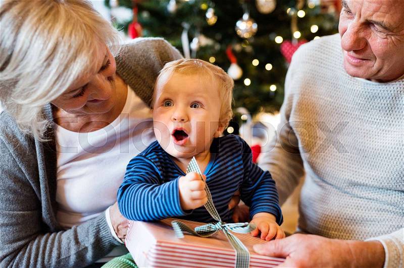 Grandparents with their little grandson at Christmas tree at home unpacking presents, stock photo