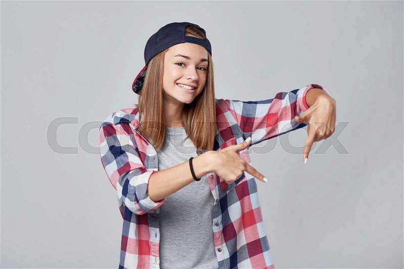 Teen girl pointing to the side down at empty copy space, over grey background, stock photo