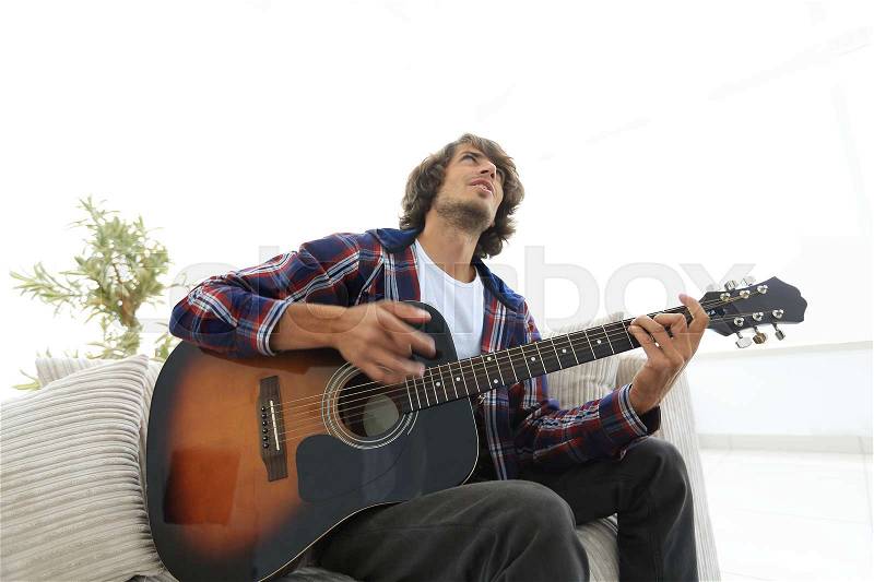 Modern guy playing guitar sitting on the couch. concept of a lifestyle. photo with copy space, stock photo