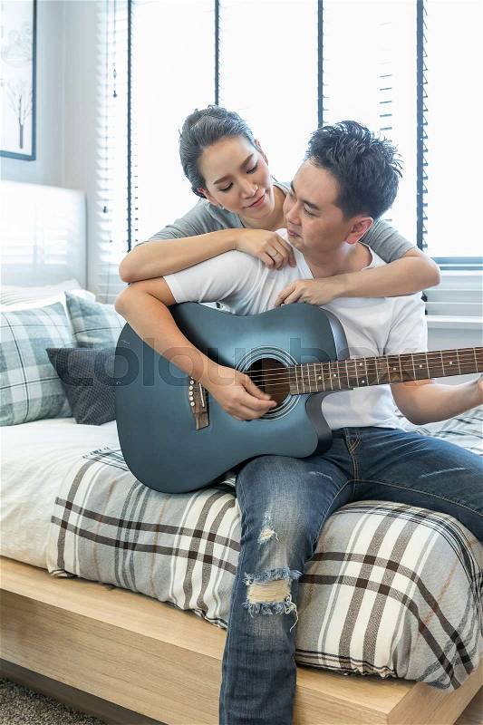 Young Couples playing guitar tohether in bedroom of contemporary house for modern lifestyle concept, stock photo