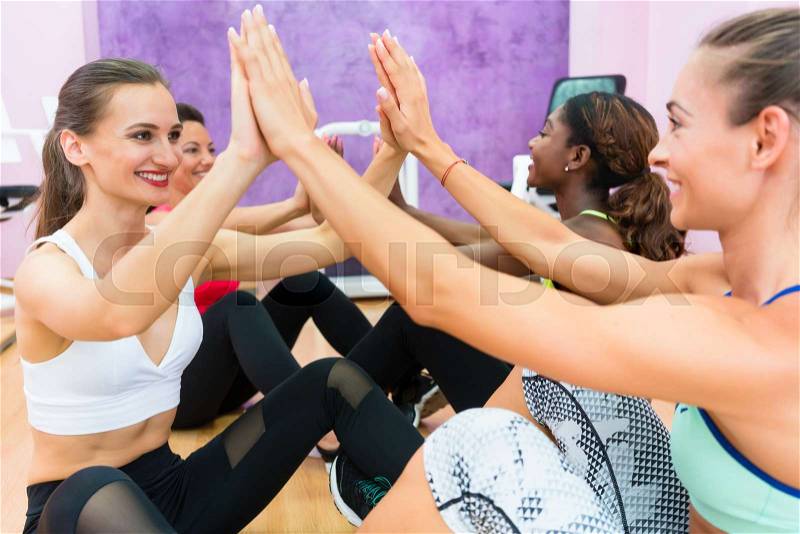 Cheerful woman clapping the hands of her workout partner after crunch exercise during group class, for core training in a modern fitness club for women only, stock photo