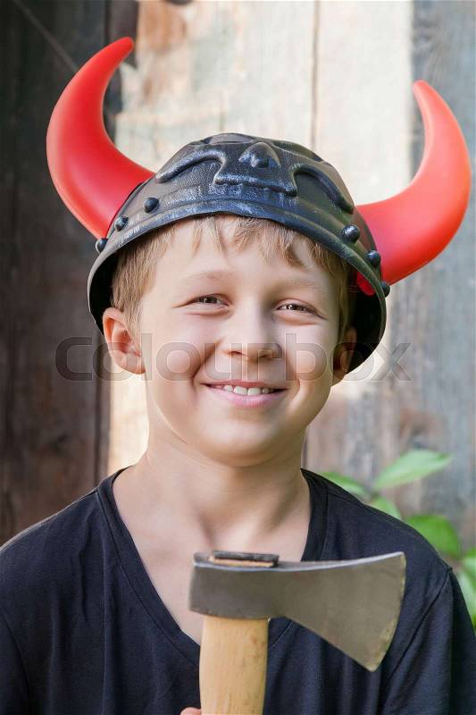 Boy in a Viking helmet with horns holds an ax outdoors, stock photo