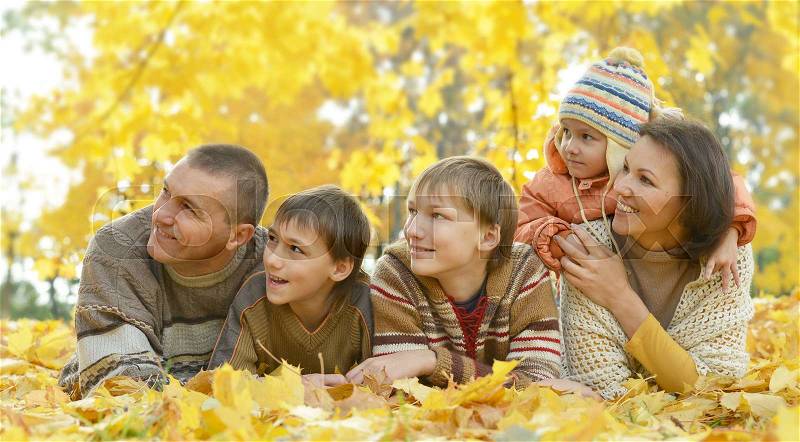 Happy smiling family lying on leaves in autumn forest, stock photo