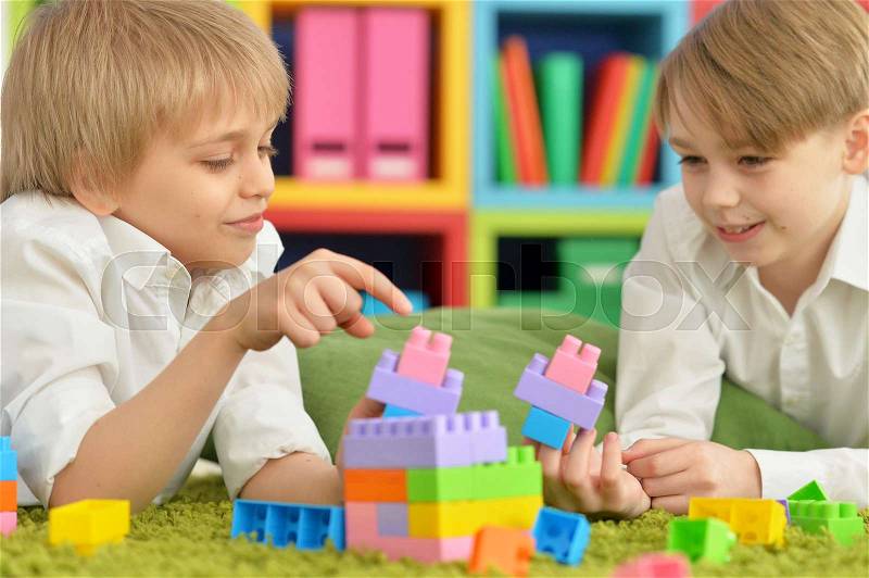 Two boys playing with colorful plastic blocks on floor, stock photo