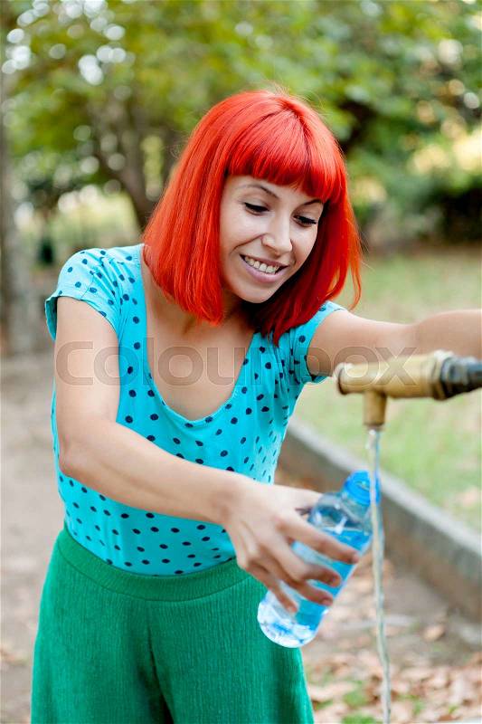 Attractive redhead girl filling a bottle of water in a fountain, stock photo