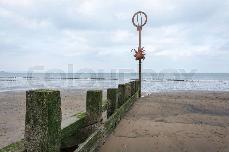 Several old wooden poles covered with moss at a beach with a metal octopus on a pole, stock photo