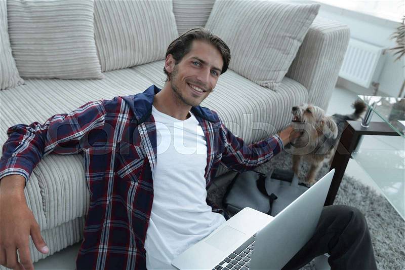 Successful guy stroking his pet sitting on the floor near the sofa in the living room. concept of a lifestyle, stock photo