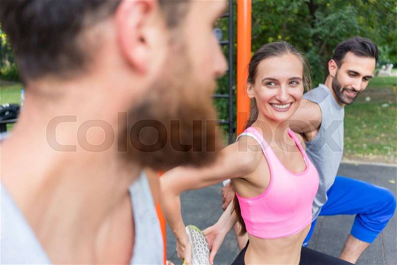Attractive fit woman smiling during stretching workout routine while exercising with her positive friends in a modern fitness park, stock photo