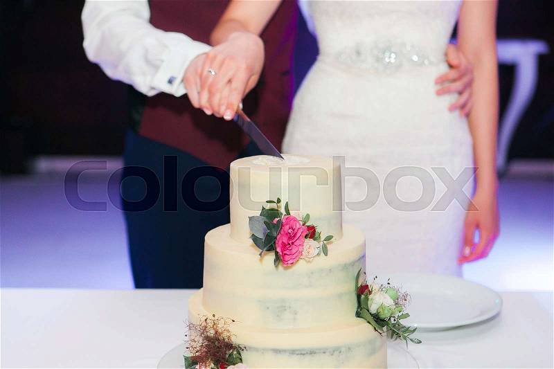 Bride and Groom at Wedding Reception Cutting the Wedding Cake with flowerd on it, stock photo
