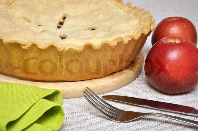 Home-baked apple pie with two red apples, fork and knife, stock photo