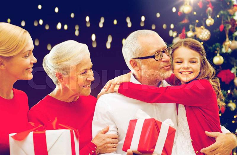Family, holidays and people concept - happy grandparents, granddaughter and mother with gift boxes and christmas thee over lights background, stock photo