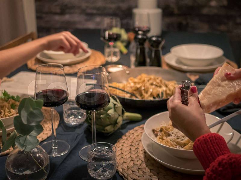 Late night dinner at home. Friends eating pasta and drinks wine at table, stock photo