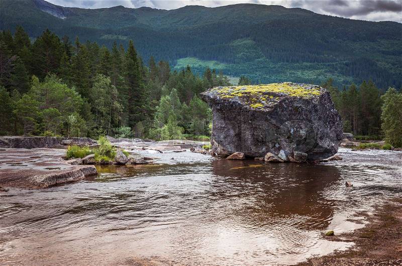 Big rock in a river in norway with background of mountains and green forest, stock photo