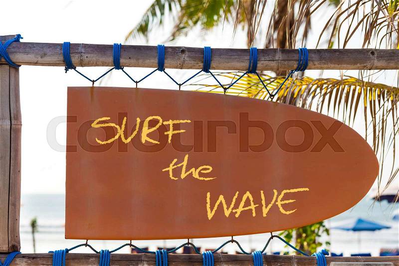 Orange vintage signboard in shape of surfboard with Surf the Wave text and palm tree in background. Vacation and travel concept, stock photo