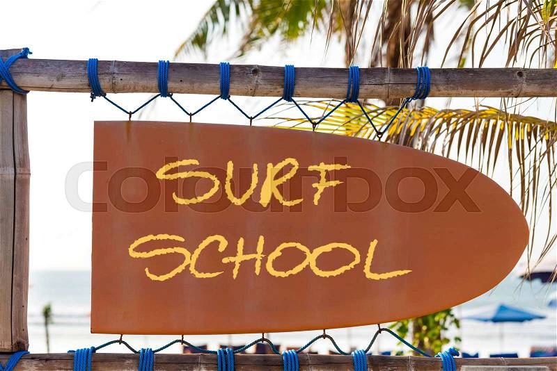 Orange vintage signboard in shape of surfboard with Surf School text and palm tree in background. Vacation and travel concept, stock photo