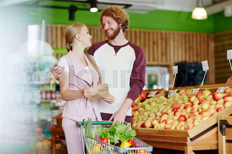 Affectionate couple with shopping list buying products in hypermarket, stock photo