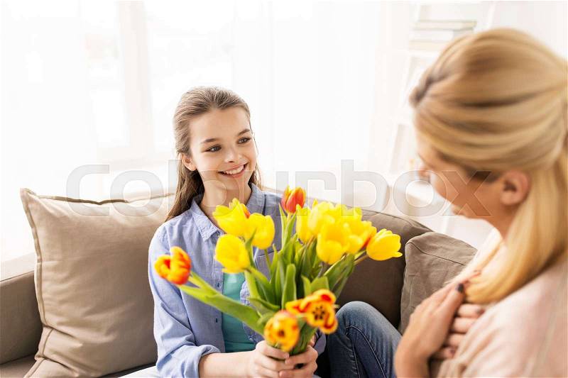 People, family and holidays concept - happy girl giving tulip flowers to her mother at home, stock photo
