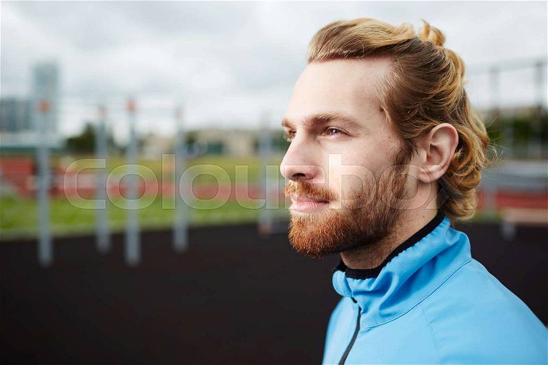 Young sportsman or professional trainer in activewear looking forward outdoors, stock photo
