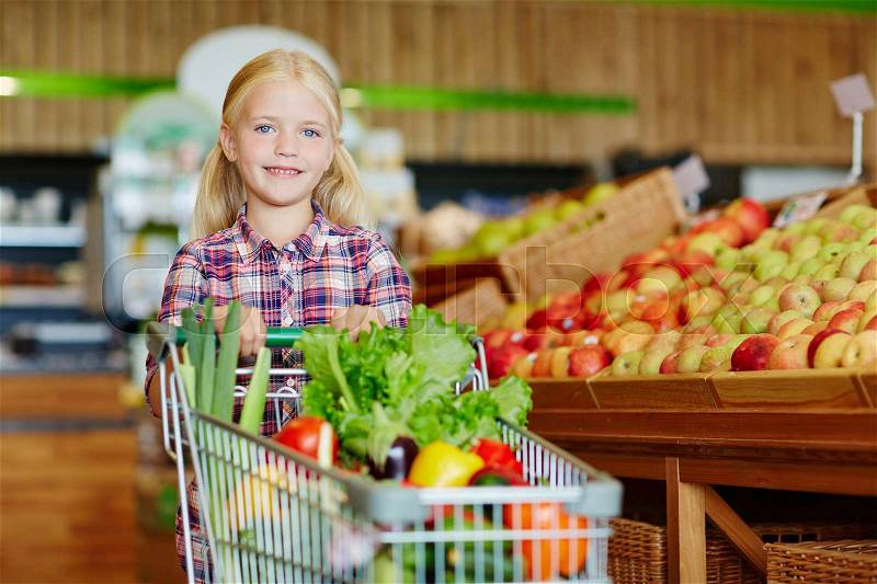 Cute little shopper with cart full of organic products looking at camera, stock photo