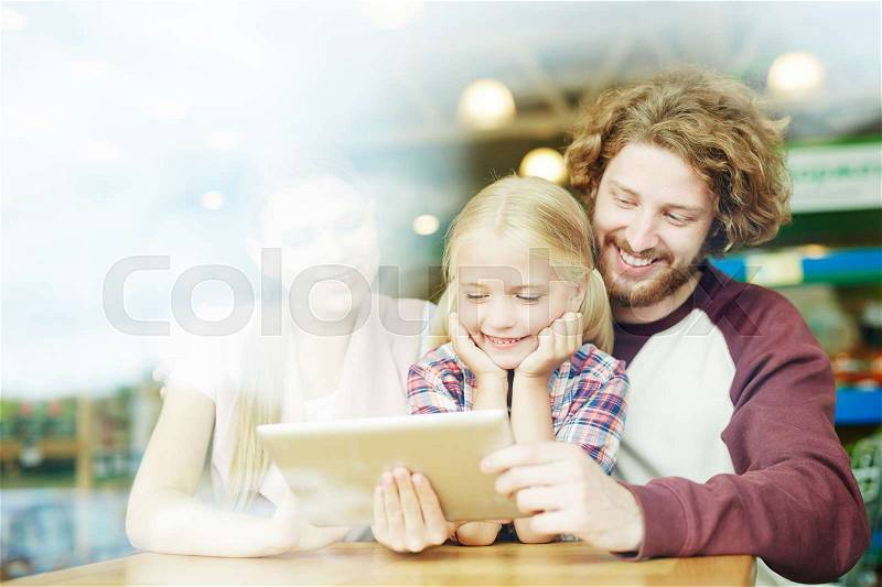 Cheerful parents and their daughter watching curious and funny video in tablet at leisure, stock photo