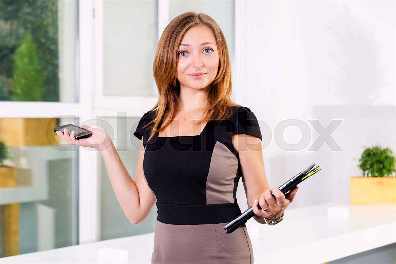 Young businesswoman in modern bright office holding the tablet and smartphone with a list of tasks. Free space for text. Business concept of office work, stock photo