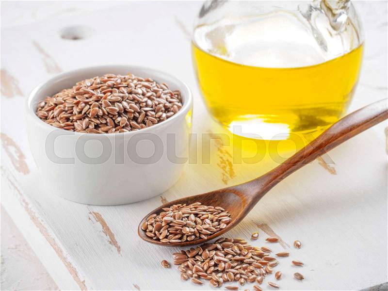 Brown flax seeds in spoon and flaxseed oil in glass bottle on white wooden background. Flax oil is rich in omega-3 fatty acid, stock photo