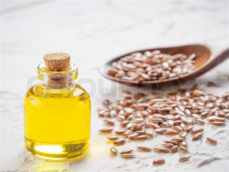 Brown flax seeds in spoon and flaxseed oil in glass bottle on white concrete background. Flax oil is rich in omega-3 fatty acid. Copy space, stock photo