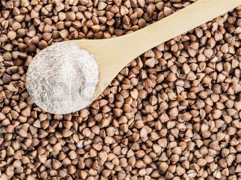Buckwheat flour in wooden spoon and buckwheat grains. Whole-grain buckwheat flour on buckwheat grains background. Copy space. Top view or flat lay, stock photo
