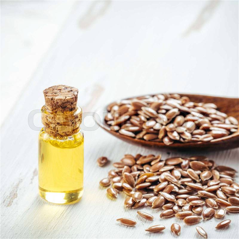 Brown flax seeds in spoon and flaxseed oil in glass bottle on white wooden background. Flax oil is rich in omega-3 fatty acid. Copy space. Square, stock photo