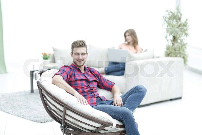Smiling young male sitting in a big chair on blurred background, stock photo