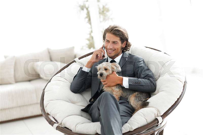 Successful businessman holds his pet and talks on the smartphone while sitting in a comfortable chair. photo with copy space, stock photo