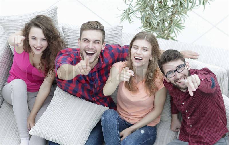 View from the top.a group of laughing friends sitting on sofa and showing forefinger on the camera, stock photo