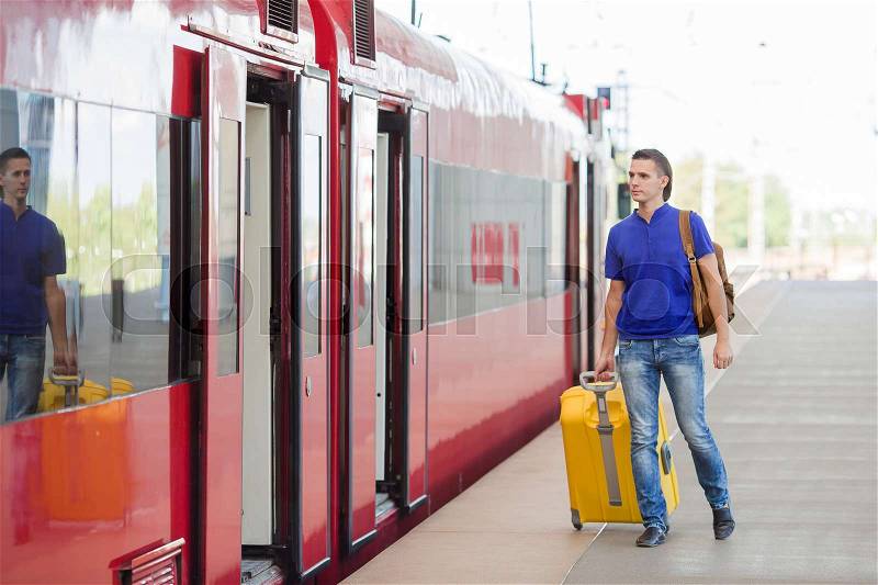 Young caucasian man with luggage at station traveling by train, stock photo