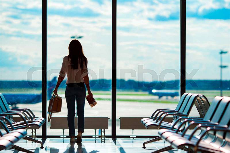 Young woman in international airport with her luggage background big window. Airline passenger in an airport lounge waiting for flight aircraft, stock photo