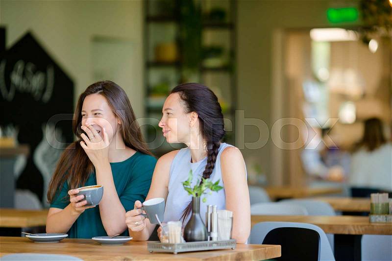 Happy smiling young women with coffee cups at cafe. Communication and friendship concept, stock photo