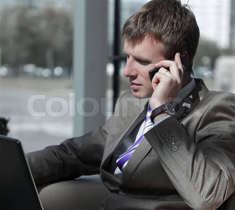 Attractive european guy talking on phone while using laptop, stock photo