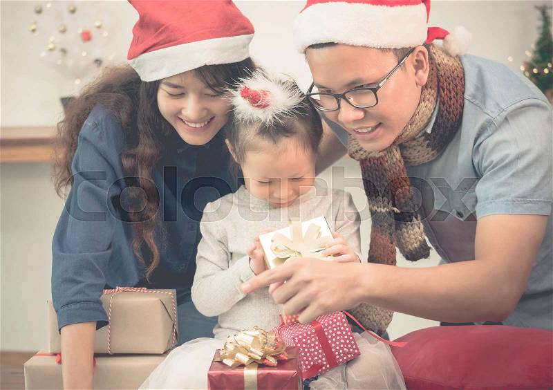 Happy family Asia family wear santa claus hat unwrap Christmas gift box at house xmas party,Holiday celebrating festive concept,vintage filter, stock photo