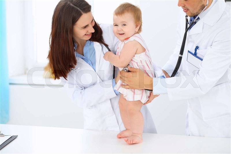 Happy cute baby at health exam at doctor\'s office. Toddler girl is standing while have been keeping by two doctors, stock photo