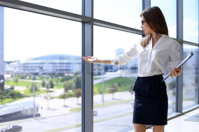 Modern business woman points to the city through the window while standing in the office, stock photo