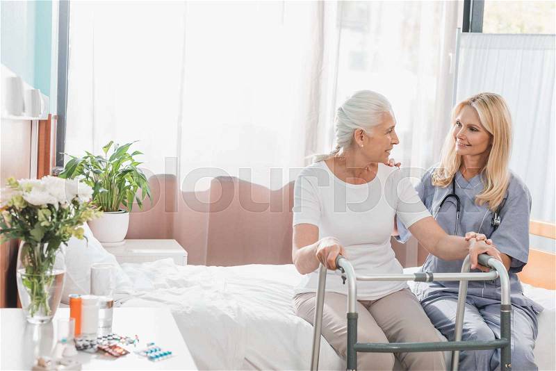 Nurse and senior patient with walker smiling each other in hospital, stock photo
