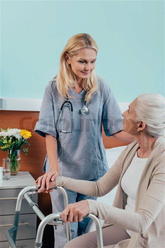 Smiling nurse looking at senior patient with walker, stock photo