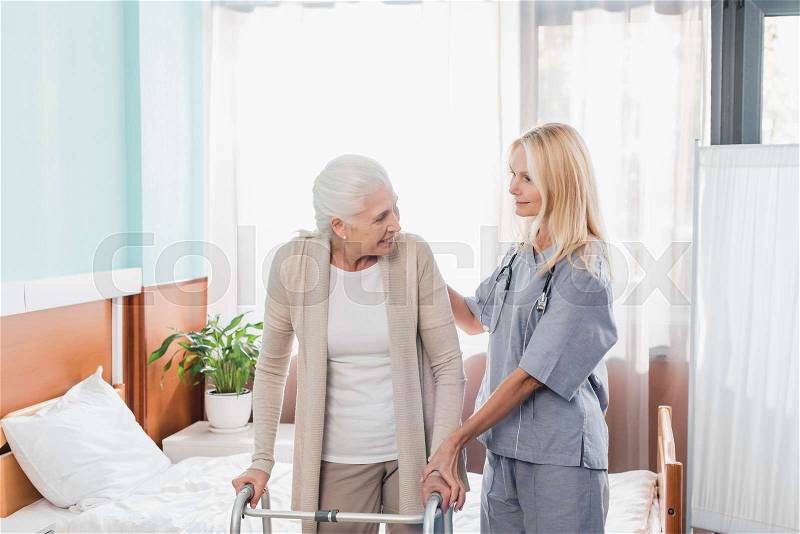 Nurse and senior woman with walker smiling each other in hospital room , stock photo